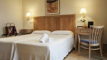 A hotel room with two beds, a wooden headboard, a desk with a chair, a lamp, and a framed picture on the wall.