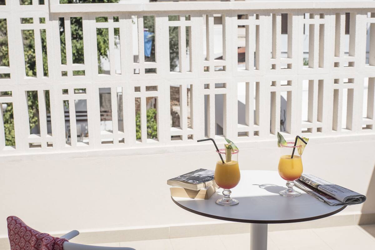 Ein Balkon mit zwei Stühlen, einem kleinen runden Tisch und zwei Getränken.