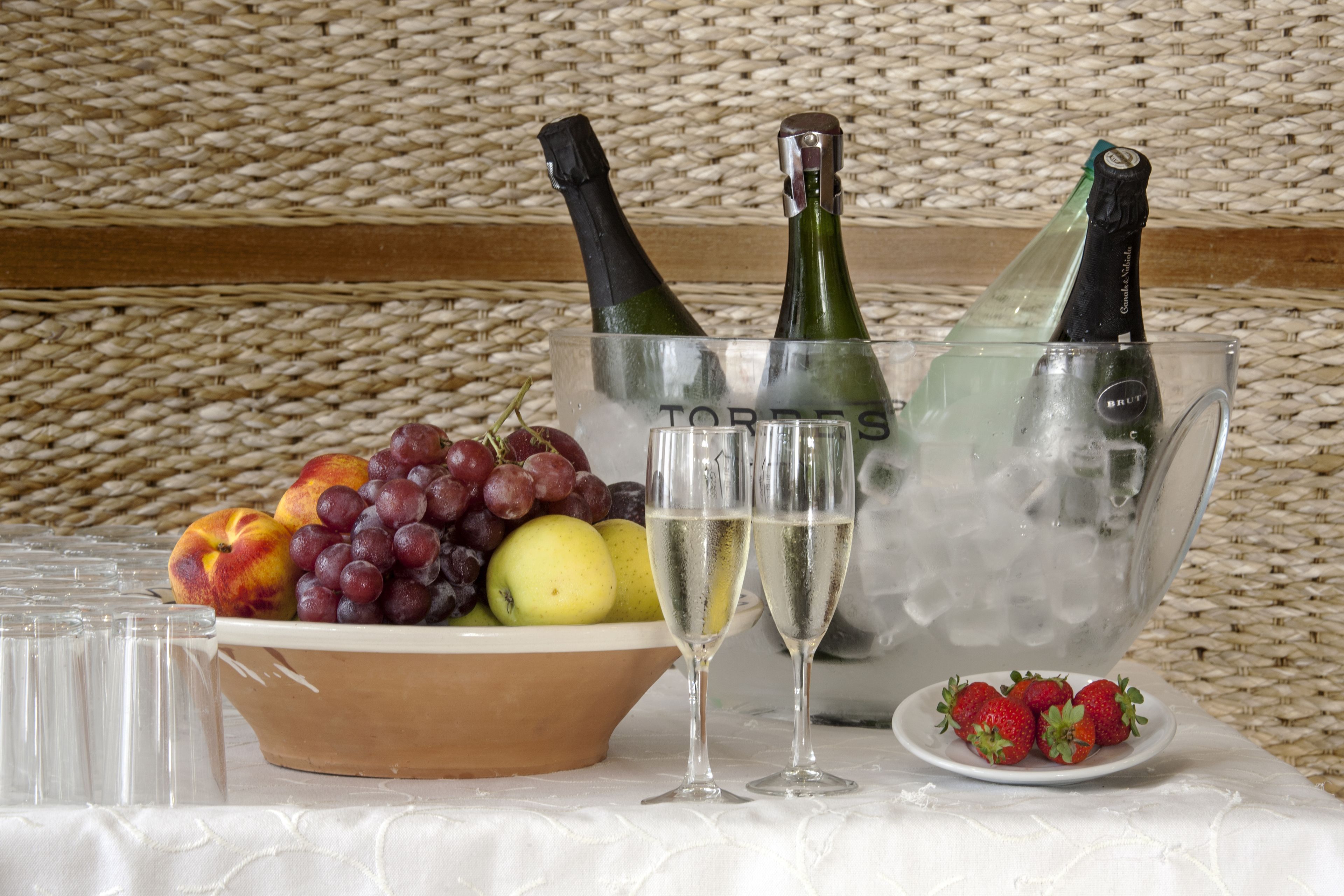 Uma mesa com uma tigela de frutas, duas garrafas de champanhe em balde de gelo e dois taças de champanhe.