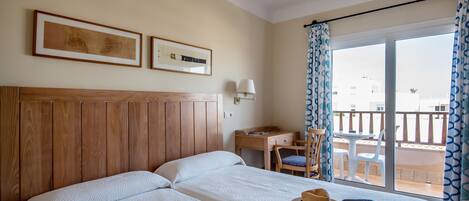 Habitación de hotel con una cama grande, un escritorio y un balcón con sillas.