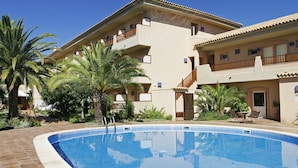 Un hotel amb piscina, diversos balcons i palmeres.