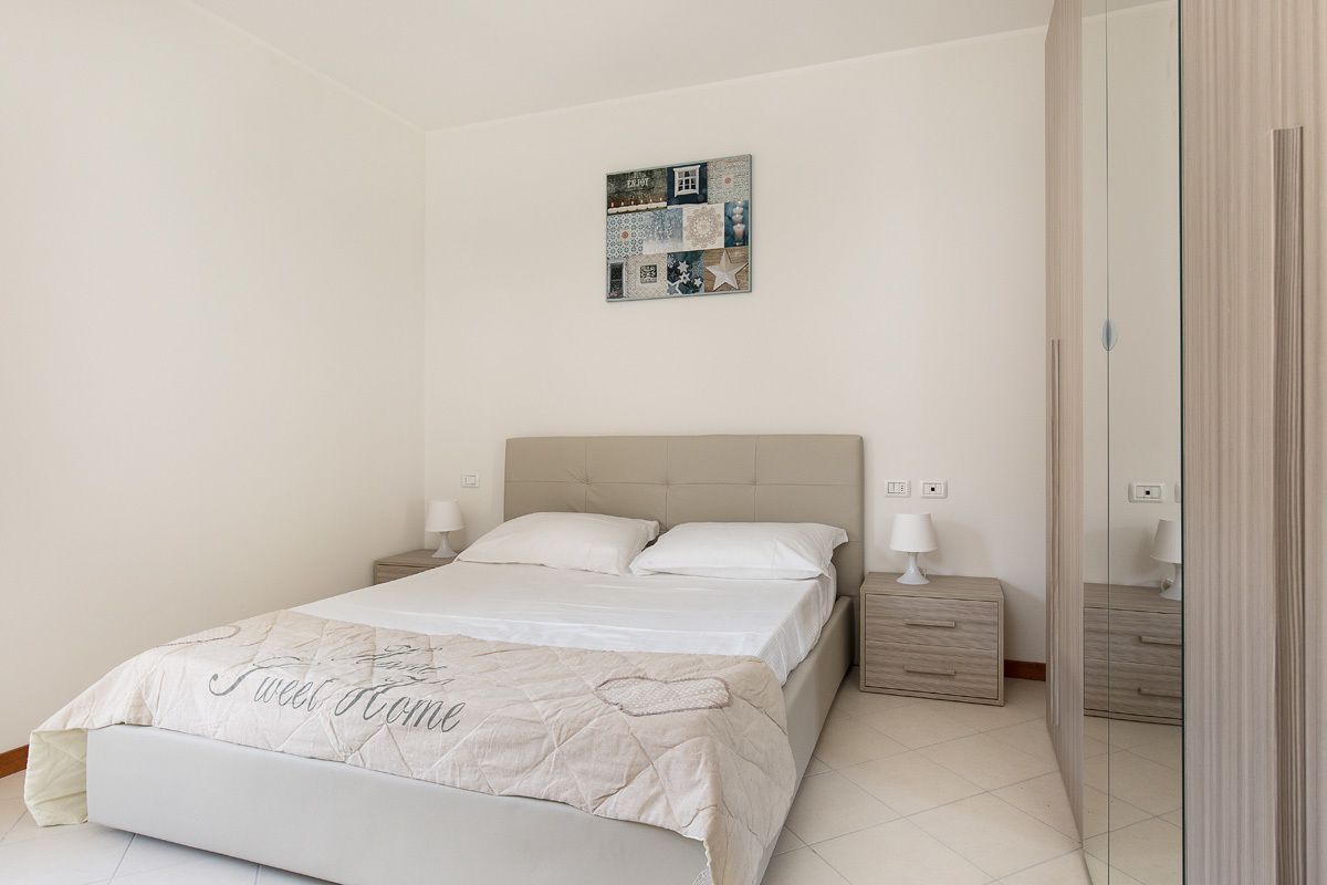 Een slaapkamer met een bed, nachtkastjes, een spiegel en een decoratie aan de muur.