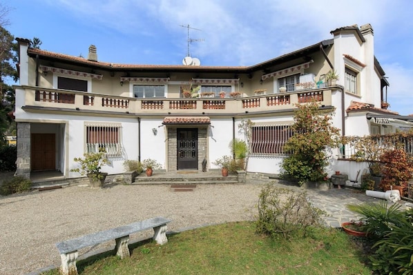 A two-story building with a courtyard, featuring a stone bench, potted plants, and a tiled roof.