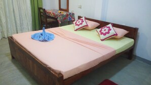 Una cama individual con estructura de madera, una colcha rosa y dos almohadones decorativos con motivos florales.
