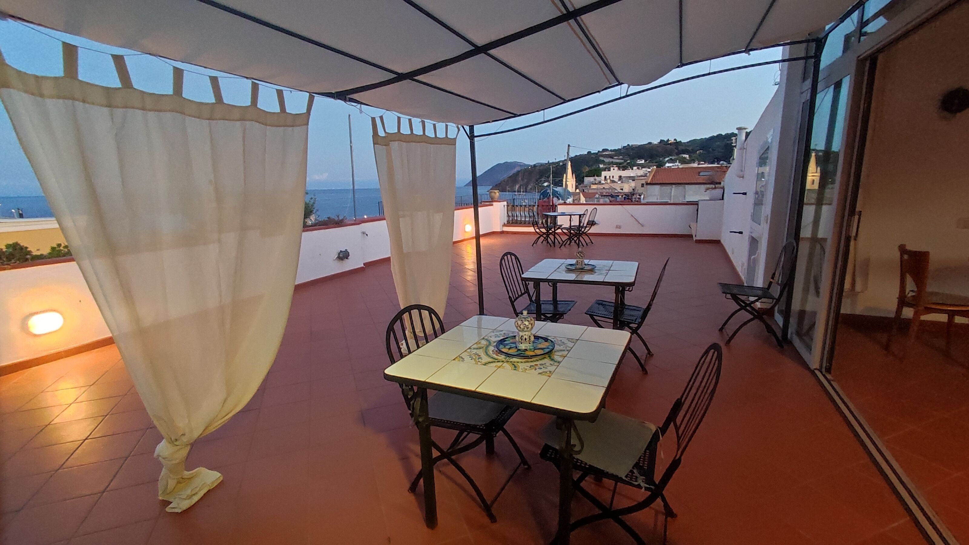 A terrace with a table and chairs, a view of the sea, and a building in the background.