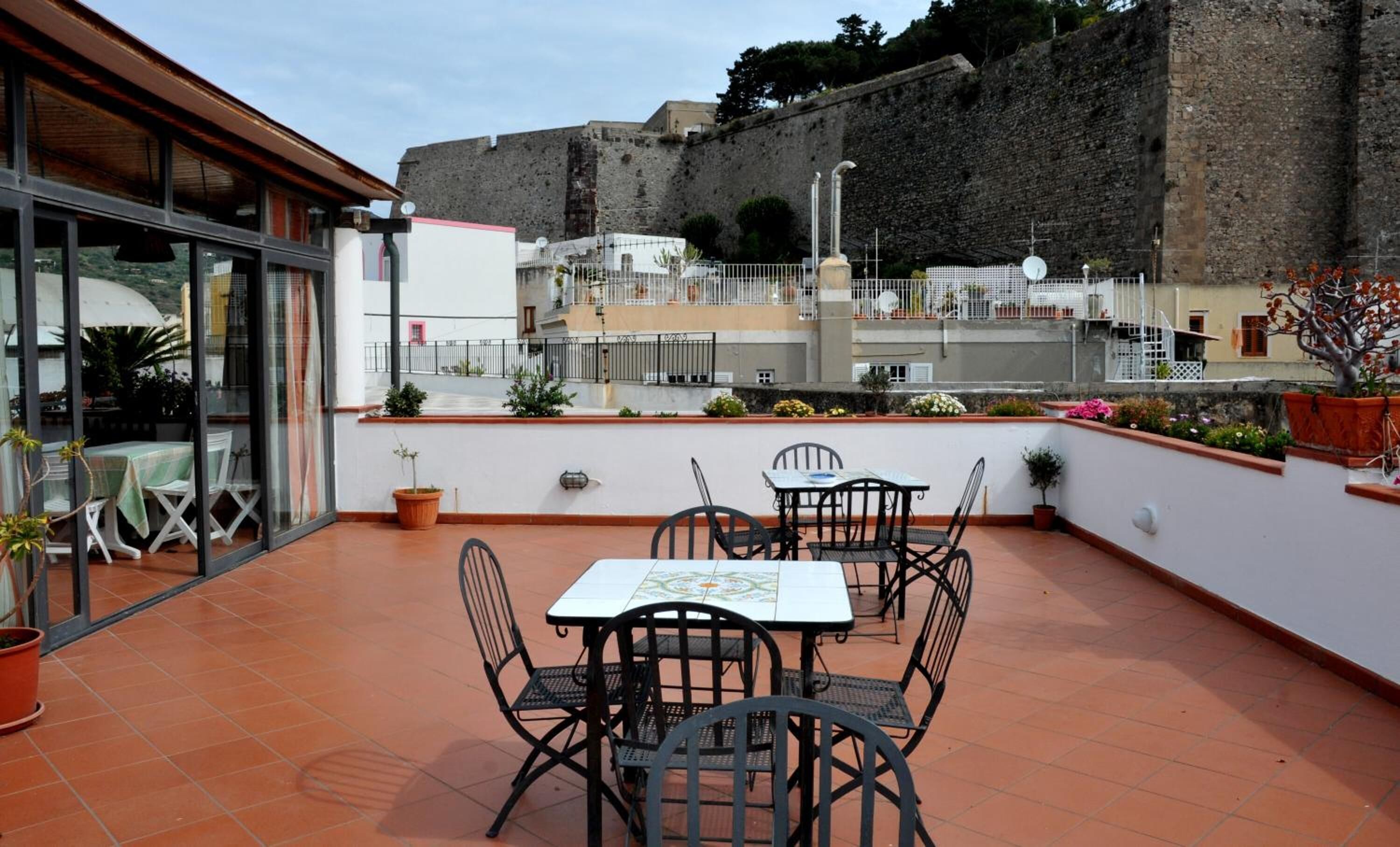 Une terrasse avec une table et des chaises, des plantes en pot et une vue sur un ancien mur de pierre.