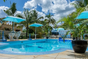 Una piscina con sombrillas azules, palmeras y mobiliario de exterior.