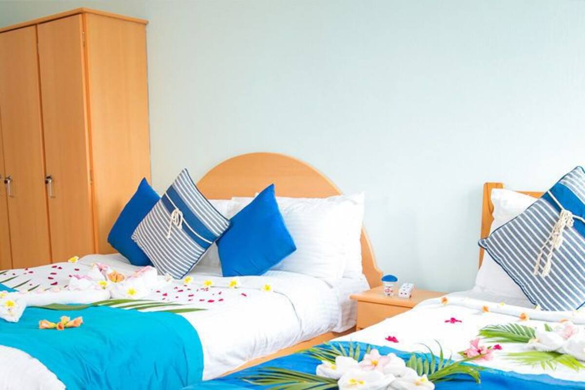 A hotel room with two beds, a wooden wardrobe, and a bathroom with a shower curtain.