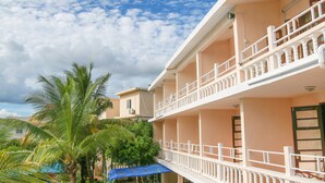 A multi-story building with balconies, a blue awning, and palm trees. - Ayati Hotels (Flic-en-Flac)