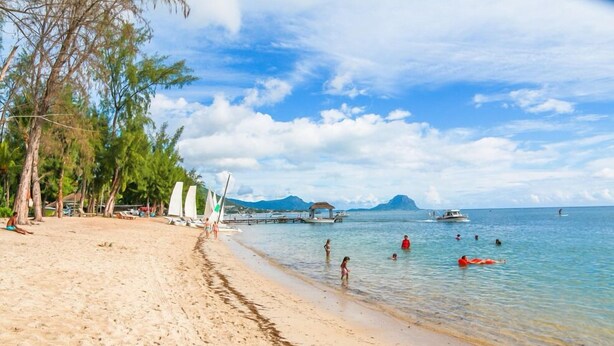 A beach with clear water, people swimming, and boats in the distance. - Ayati Hotels (Flic-en-Flac)