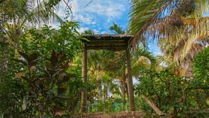 A rustic wooden structure with steps leading up to a thatched roof, surrounded by lush tropical vegetation. - Ayati Hotels (Flic-en-Flac)