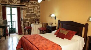 A bedroom with a stone wall, a bed with red and white bedding, a desk with a lamp, and a chair. - Rectoral de Candas (Rairiz de Veiga)