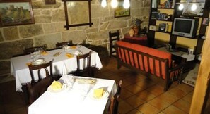 A dining area with a stone wall, a long wooden bench, and a table set for a meal. - Rectoral de Candas (Rairiz de Veiga)