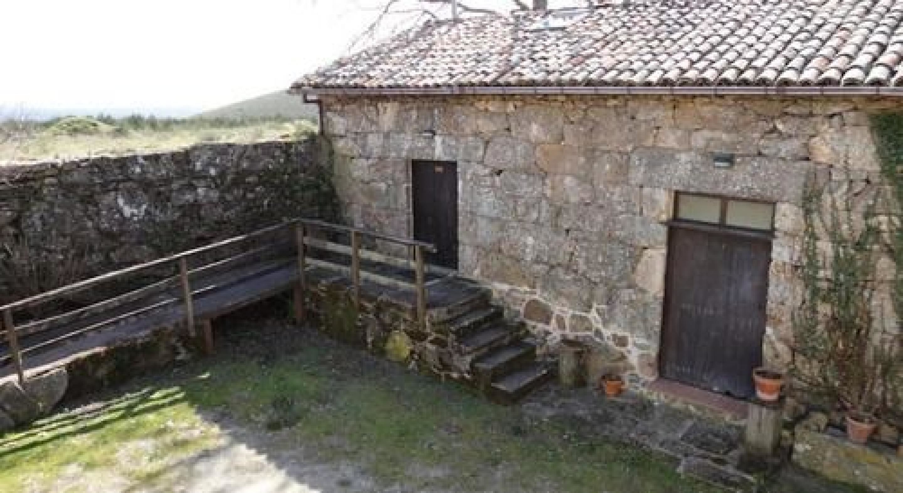 Un edificio de piedra con techo de tejas, una pequeña escalera que conduce a una puerta y una barandilla metálica.