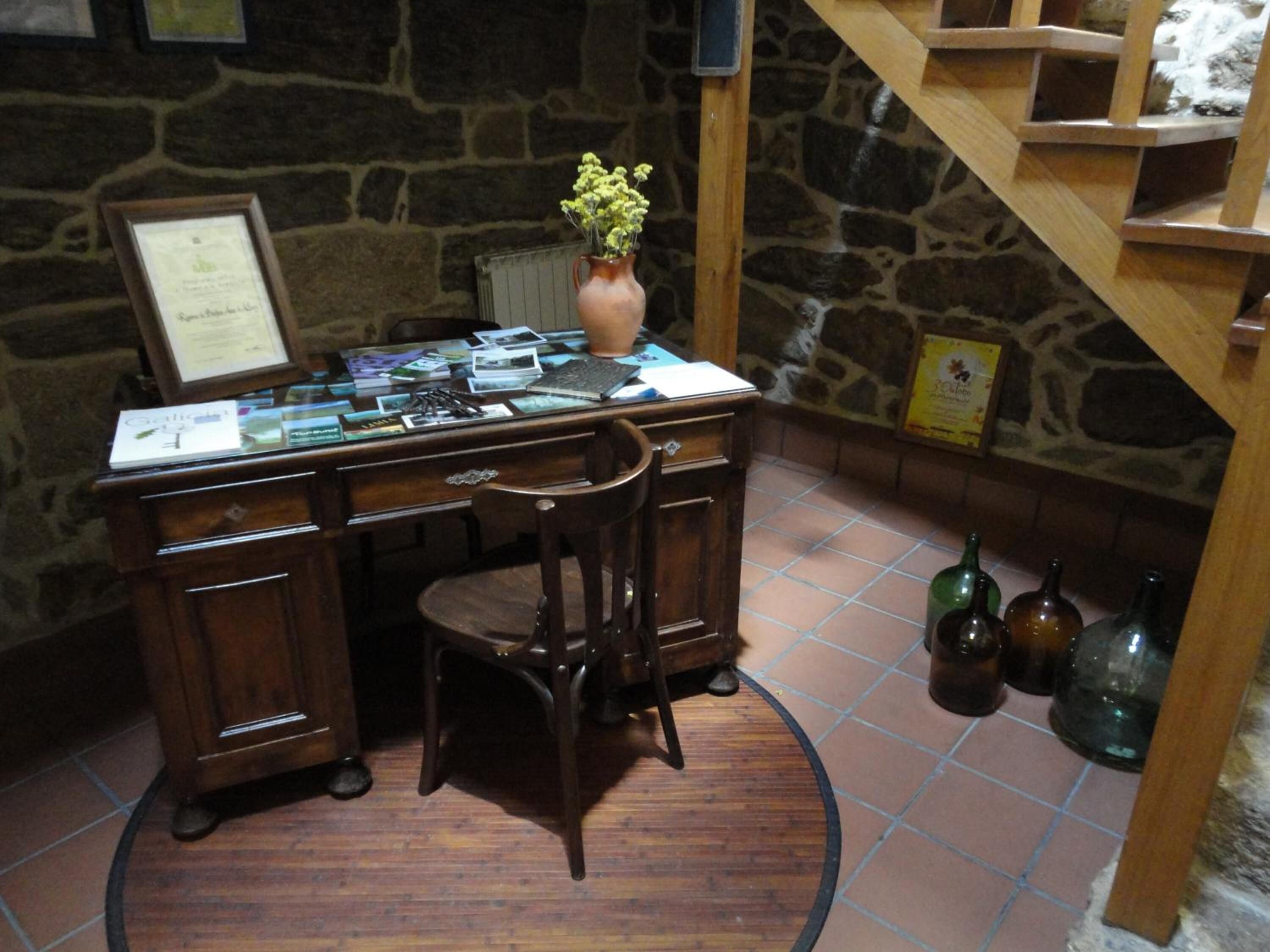 Un bureau en bois orné d’un vase de fleurs, d’un certificat encadré et de divers documents.