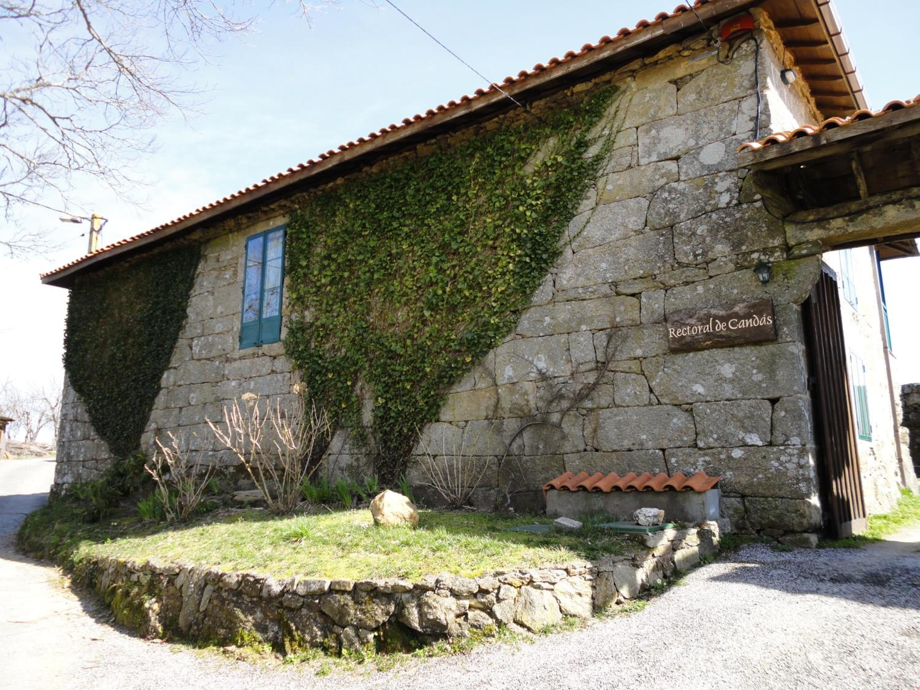 Un edificio de piedra con techo de tejas, hiedra cubriendo parte de las paredes y un letrero que dice "Rectoral de Candás".