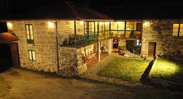 A stone house with a balcony and a well-lit interior. - Rectoral de Candas (Rairiz de Veiga)