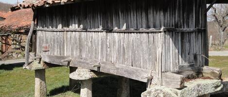 A rustic wooden structure with a tiled roof, supported by stone legs, in a grassy area.