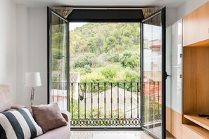 Un balcon donnant sur une colline verdoyante, un canapé avec des coussins et une lampe.
