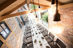 A dining area with a long table set for multiple guests, surrounded by brick walls and large windows. - Hotel Hennies (Isernhagen)