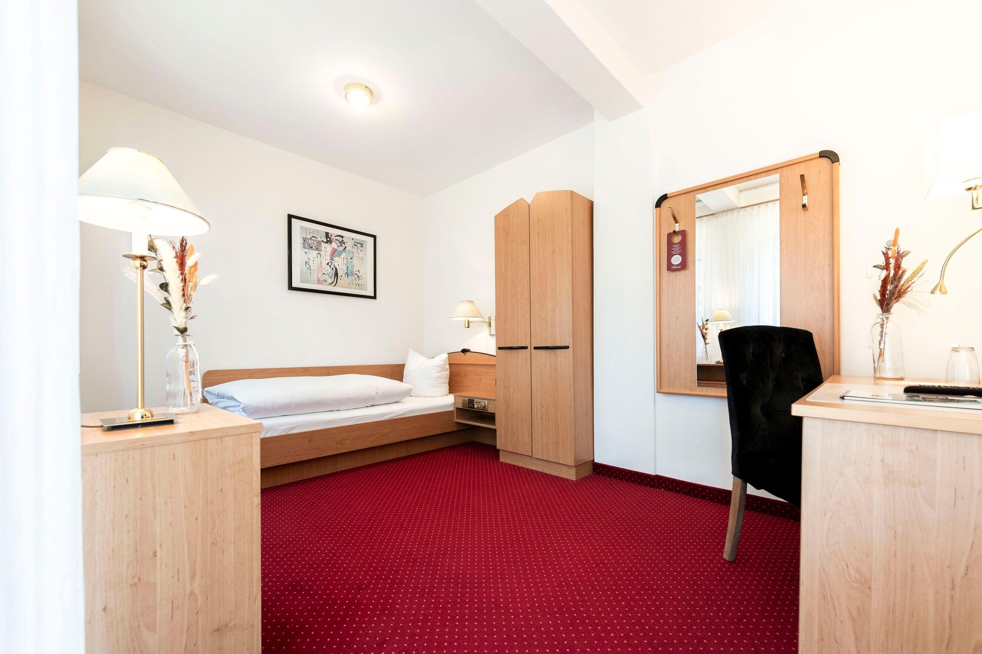 A hotel room with a bed, a desk, a wardrobe, and a mirror.