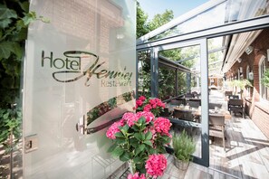 A hotel entrance with a glass door, a sign reading 'Hotel Kenning Restaurant', and outdoor seating with tables and chairs. - Hotel Hennies (Isernhagen)