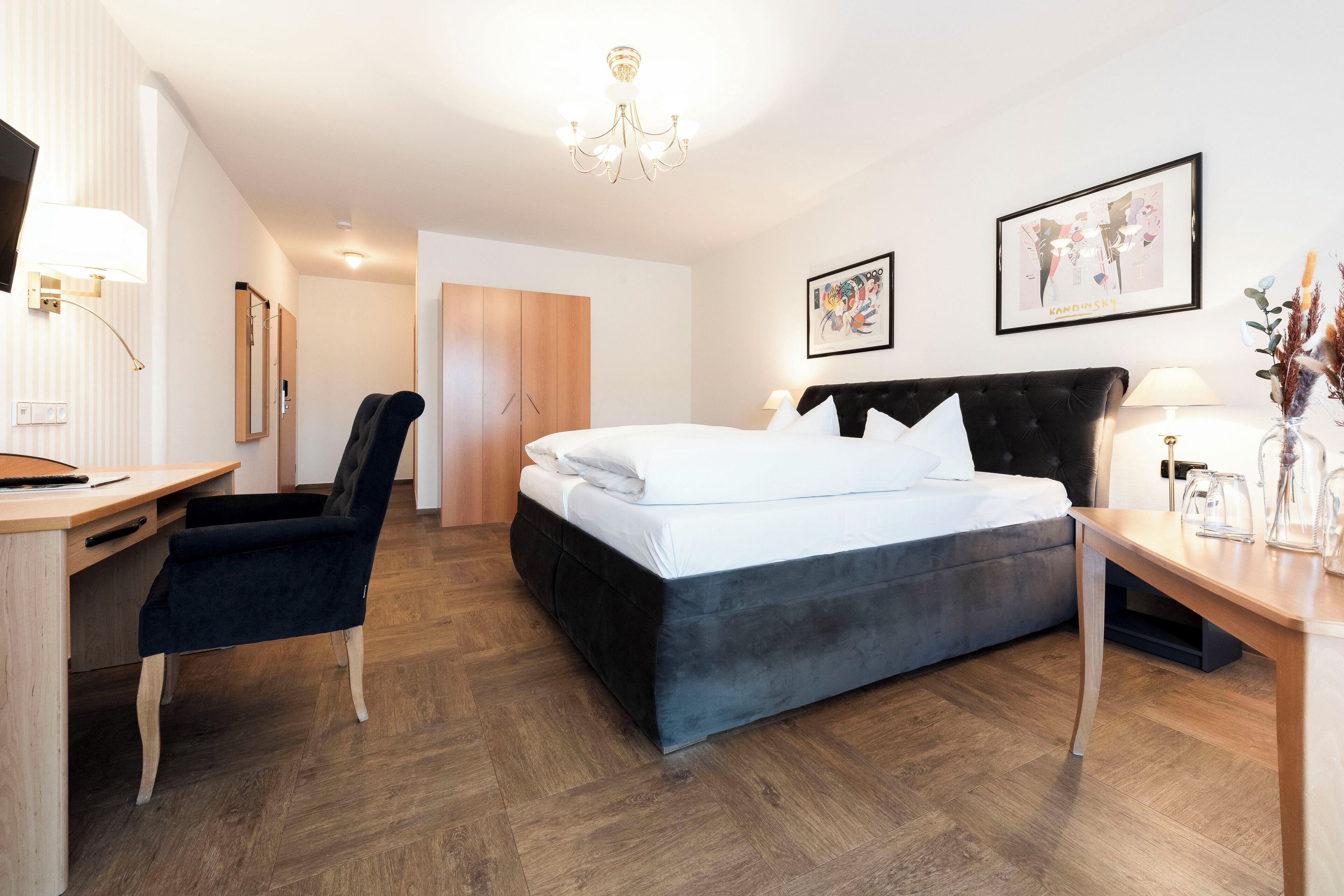 A modern hotel room with a bed, desk, chair, and a chandelier.