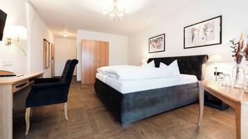 A modern hotel room with a bed, desk, chair, and a chandelier.