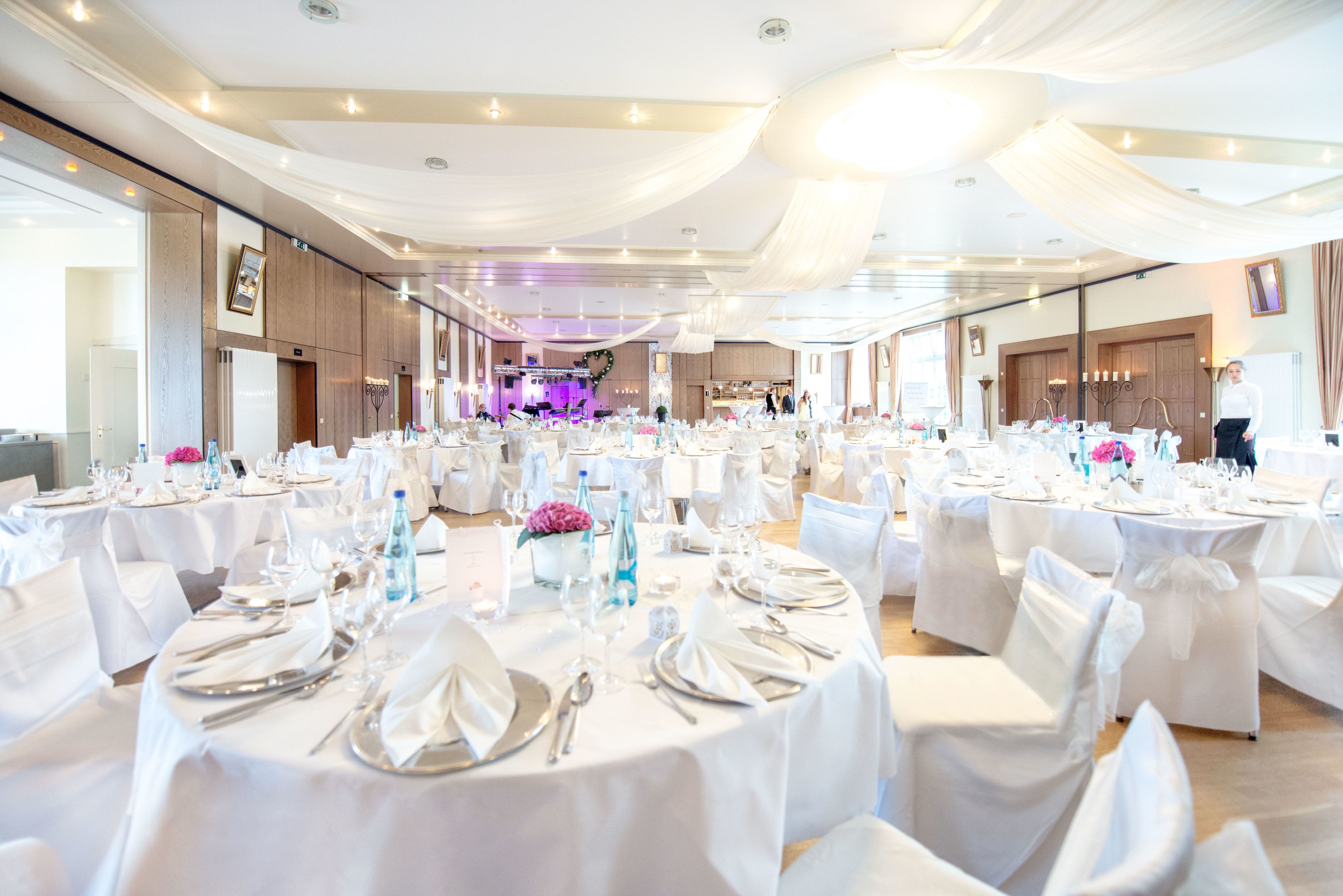 A banquet hall with round tables set for a formal event, featuring white tablecloths and silverware.