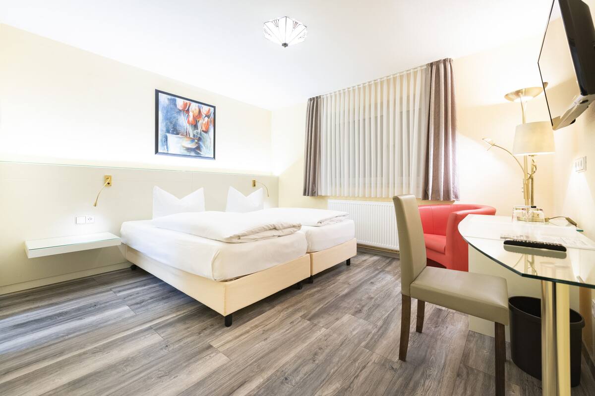 Moderni hotellihuone, jossa on sänky, työpöytä, tuoli, lamppu ja taulu seinällä.
