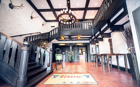 A grand staircase with a wooden railing, a chandelier, and a 'Tenne' welcome mat.