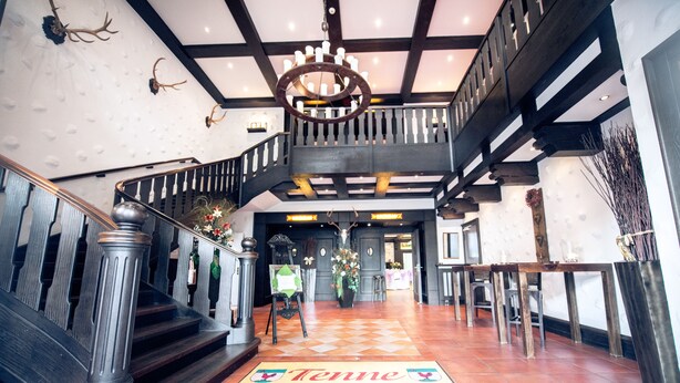 A grand staircase with a wooden railing, a chandelier, and a 'Tenne' welcome mat. - Hotel Hennies (Isernhagen)