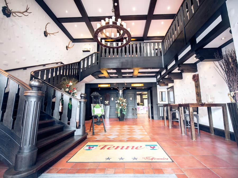 A grand staircase with a wooden railing, a chandelier, and a 'Tenne' welcome mat.