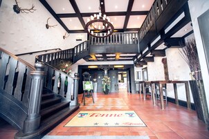 A grand staircase with a wooden railing, a chandelier, and a 'Tenne' welcome mat.