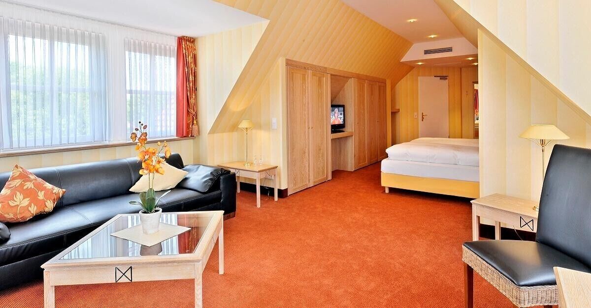 Una habitación de hotel con sofá, mesa de centro, cama, televisión y una mesita con lámpara.