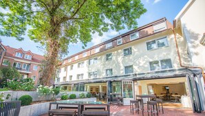 A courtyard with outdoor seating, a pool, and a building with multiple floors and large windows. - Hotel Hennies (Isernhagen)