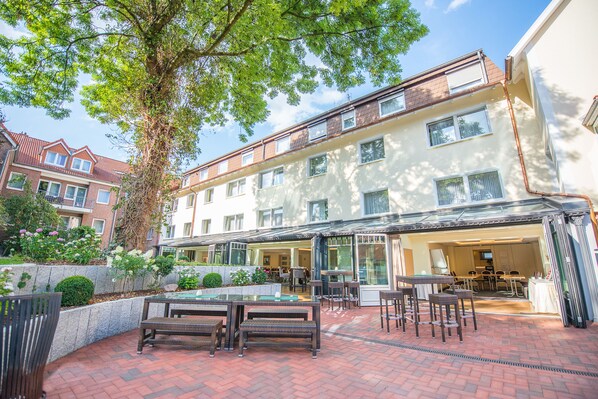 A courtyard with outdoor seating, a pool, and a building with multiple floors and large windows. - Hotel Hennies (Isernhagen)
