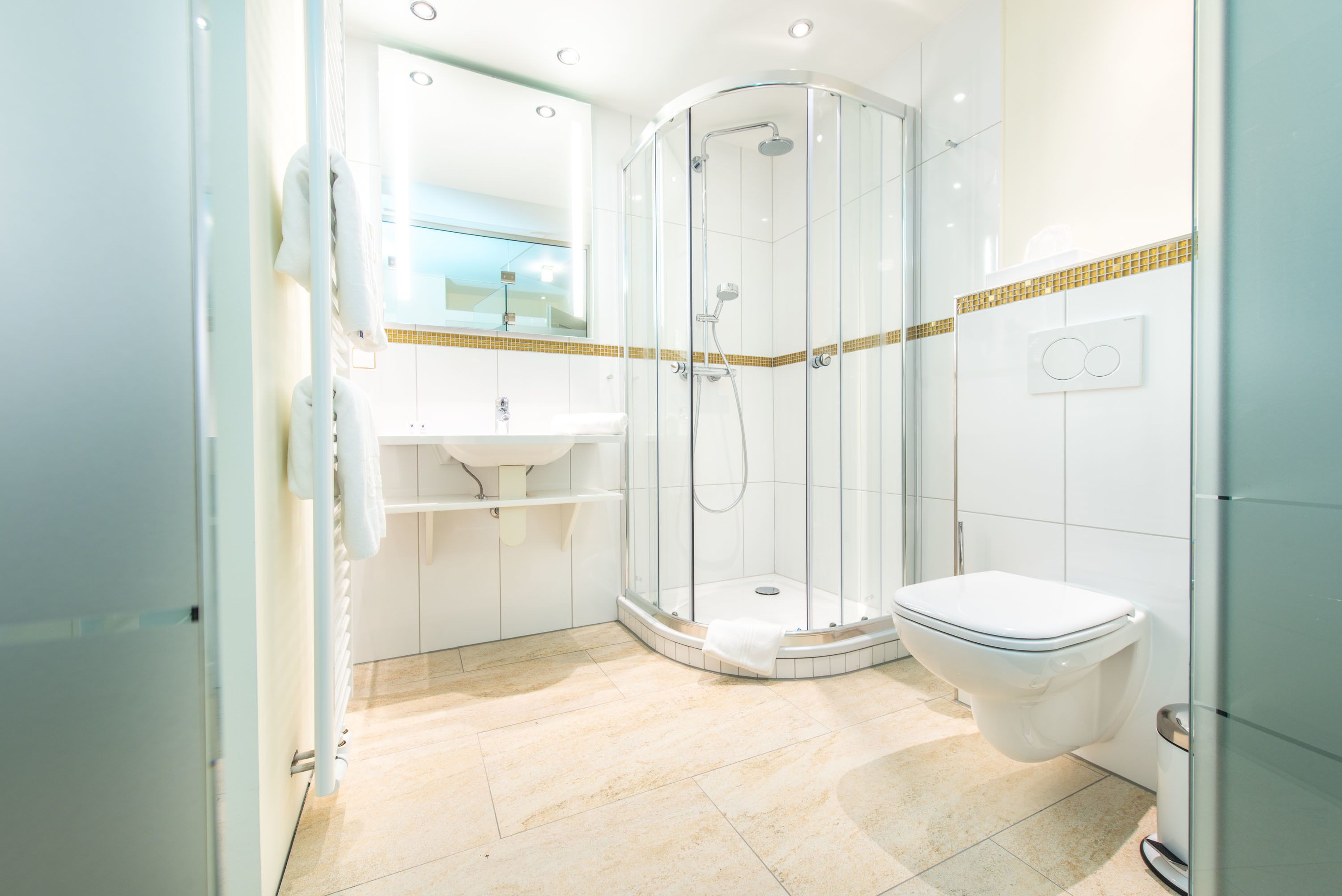 Une salle de bain moderne avec une douche à parois de verre, des toilettes blanches et un lavabo avec un miroir au-dessus.