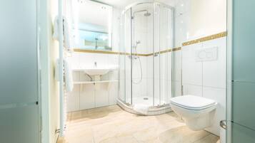 Une salle de bain moderne avec une douche à parois de verre, des toilettes blanches et un lavabo avec un miroir au-dessus.