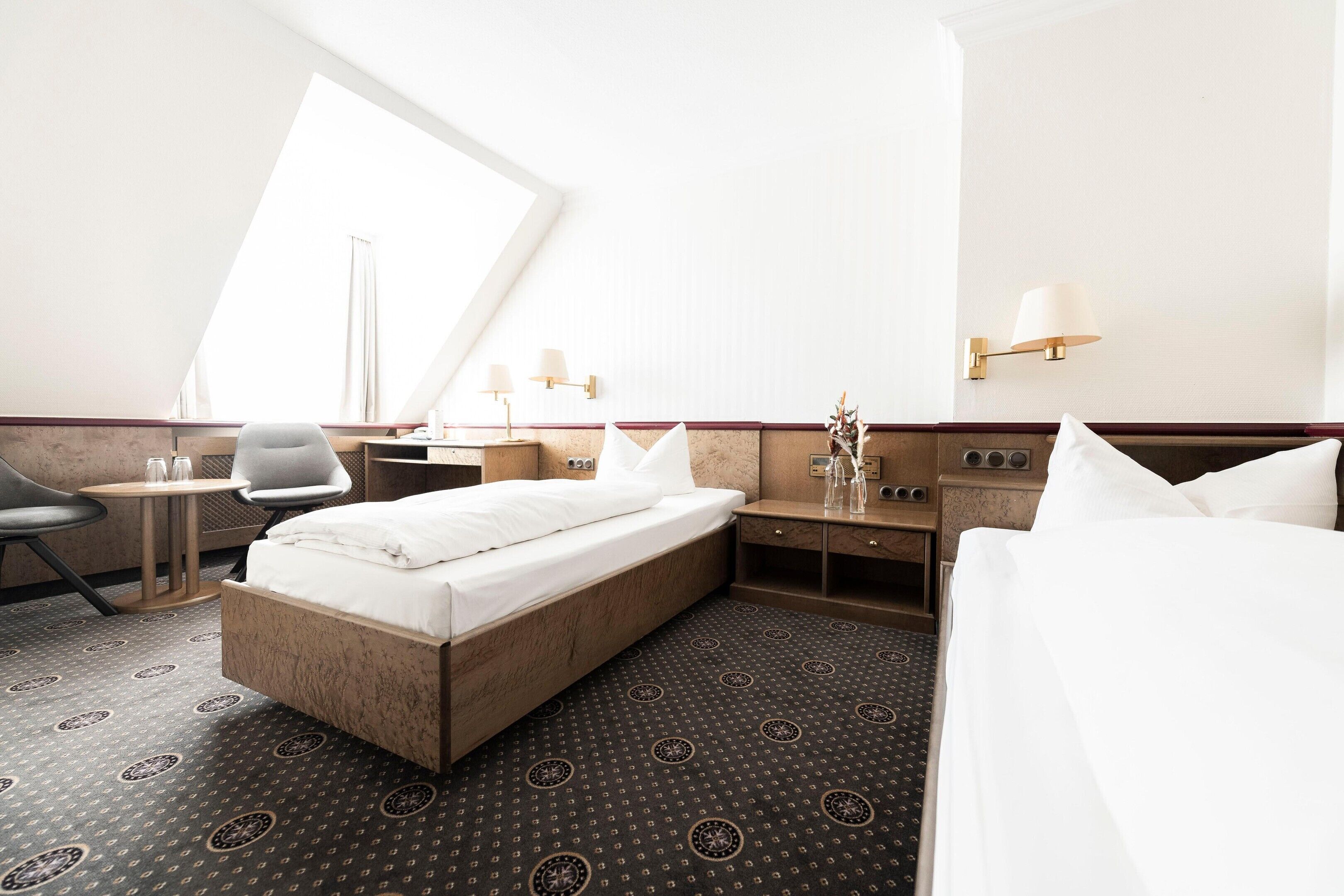 Et hotelværelse med seng, sengebord, stol og et stort vindue.