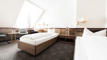 Et hotelværelse med seng, sengebord, stol og et stort vindue.