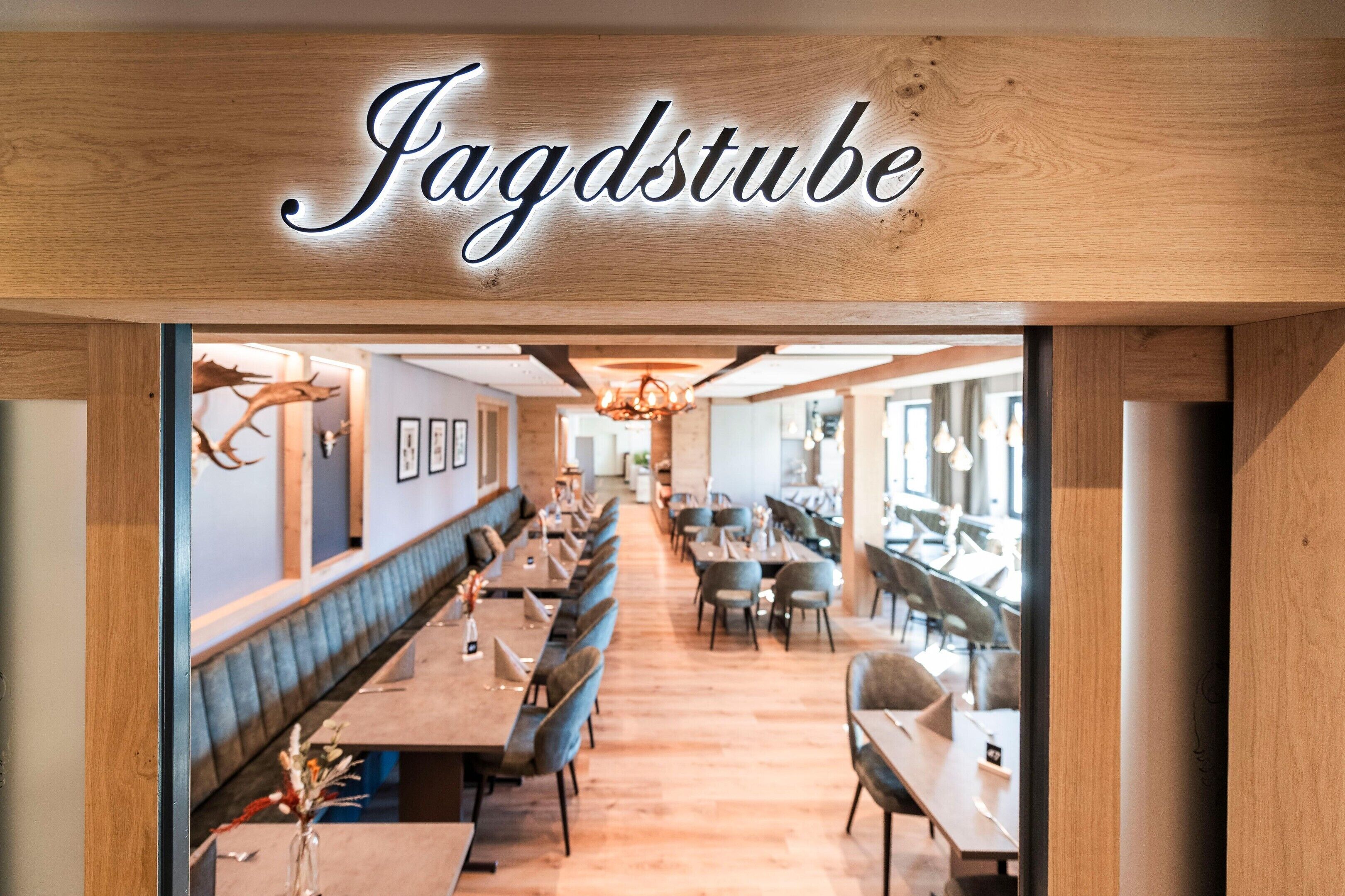 L’intérieur d’un restaurant présente un long comptoir, des banquettes et un plafond en bois sur lequel le nom « Fagdstube » est illuminé.