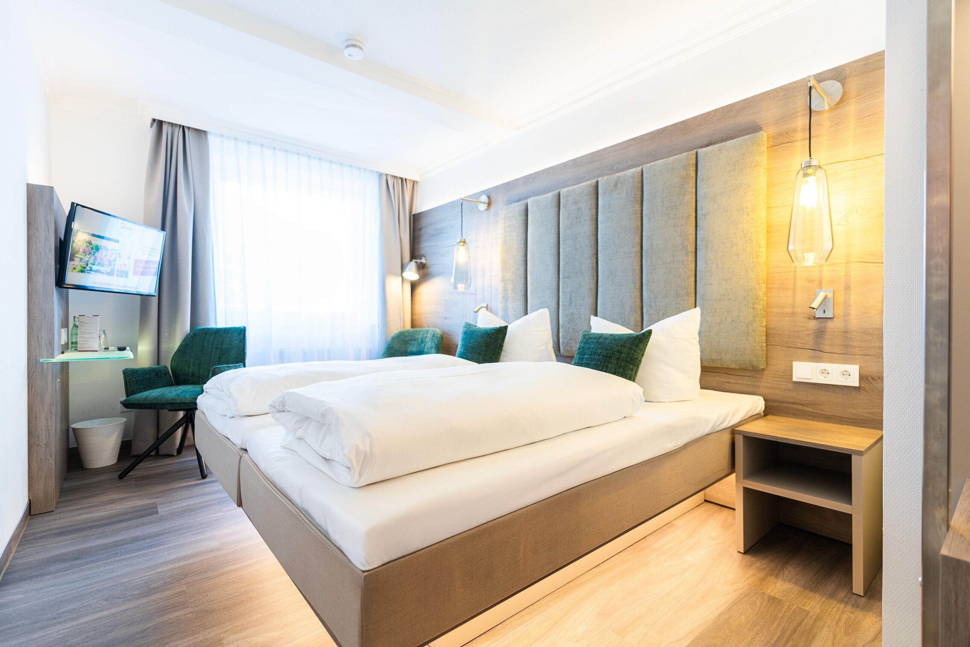 A hotel room with a large bed, a desk, a chair, a TV, and a wooden headboard.