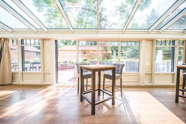 A spacious room with a large table and chairs, a skylight, and large windows offering views of the outdoors. - Hotel Hennies (Isernhagen)