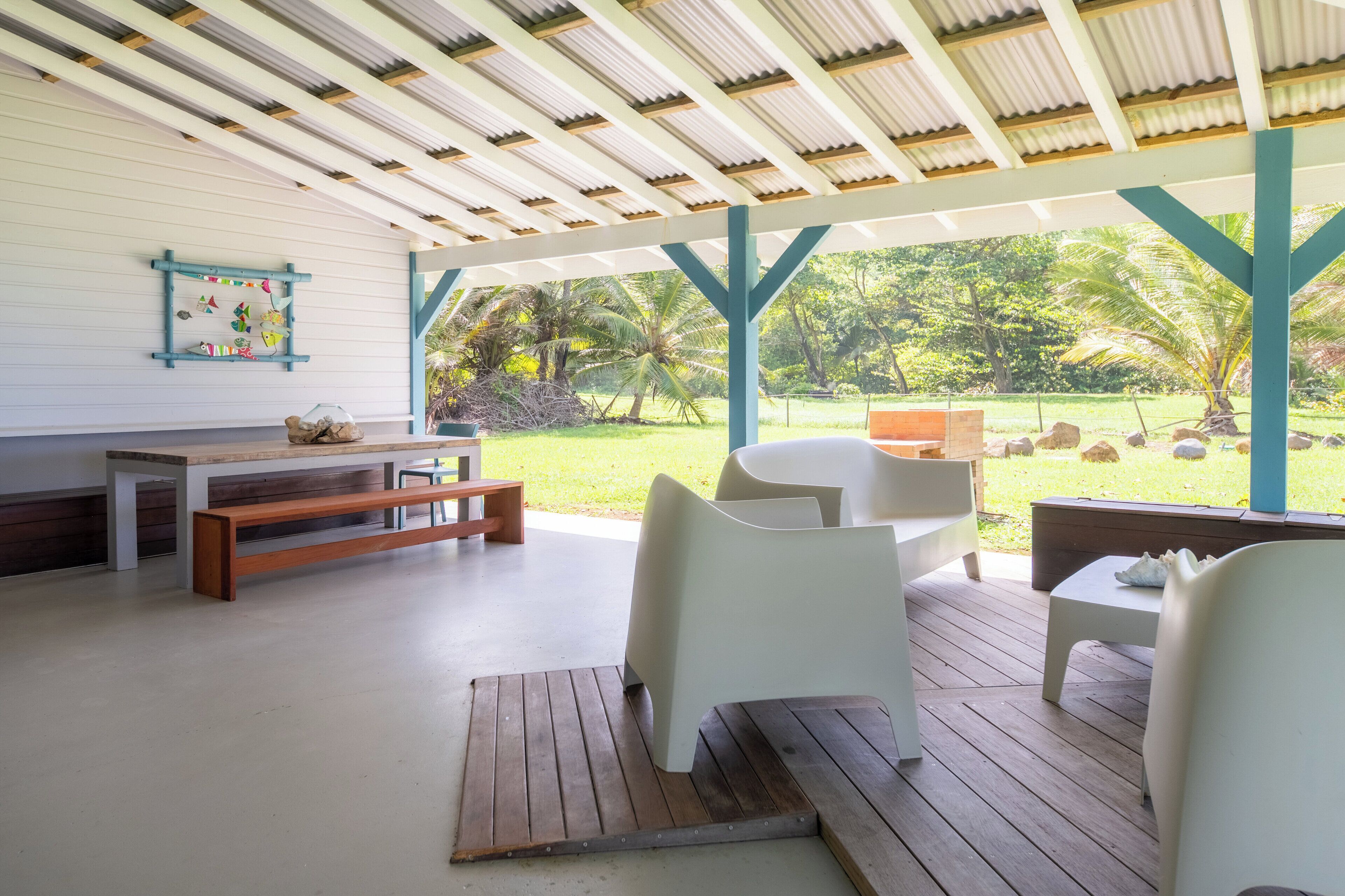 Un patio techado al aire libre con un banco de madera, sillas blancas y una mesa.