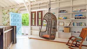 Una habitación con una silla colgante, un sillón mecedor y una estantería llena de libros y juegos.