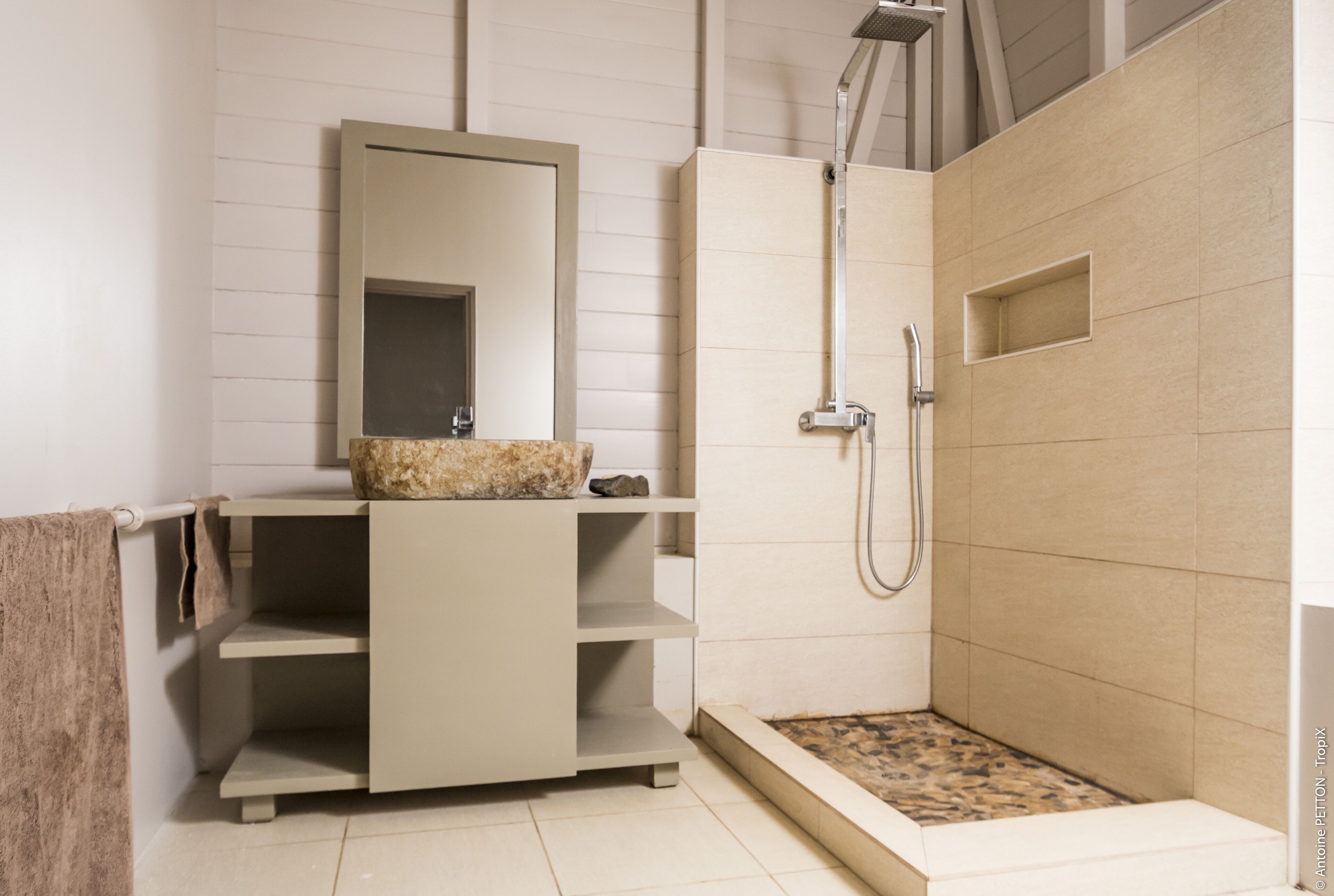 A modern bathroom with a built-in shower, a vanity with a mirror, and a stone basin.