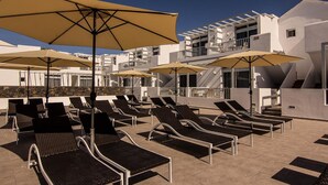 A rooftop pool area with sun loungers and umbrellas, white buildings, and a clear sky. - Home from home 2 bed luxury apartment, heated pool. 202 (Puerto Del Carmen)