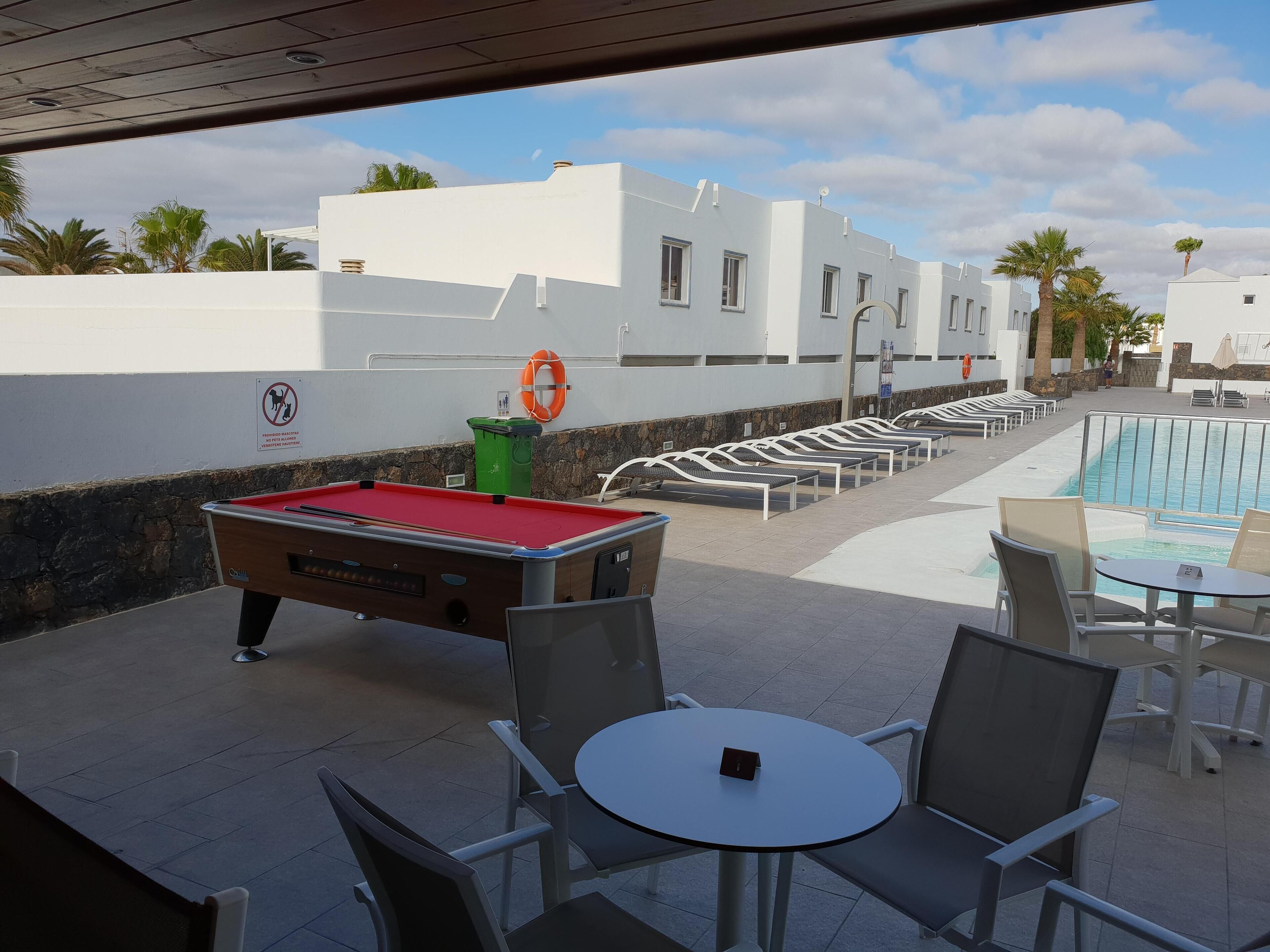 Een zwembadterras met een pooltafel, ligbedden en een zwembad.