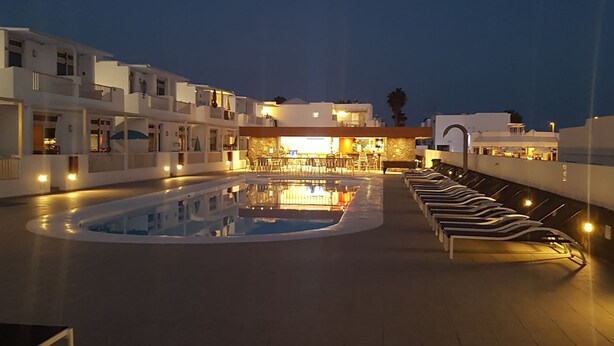 A pool area with lounge chairs and a building with multiple balconies in the background. - Home from home 2 bed luxury apartment, heated pool. 202 (Puerto Del Carmen)